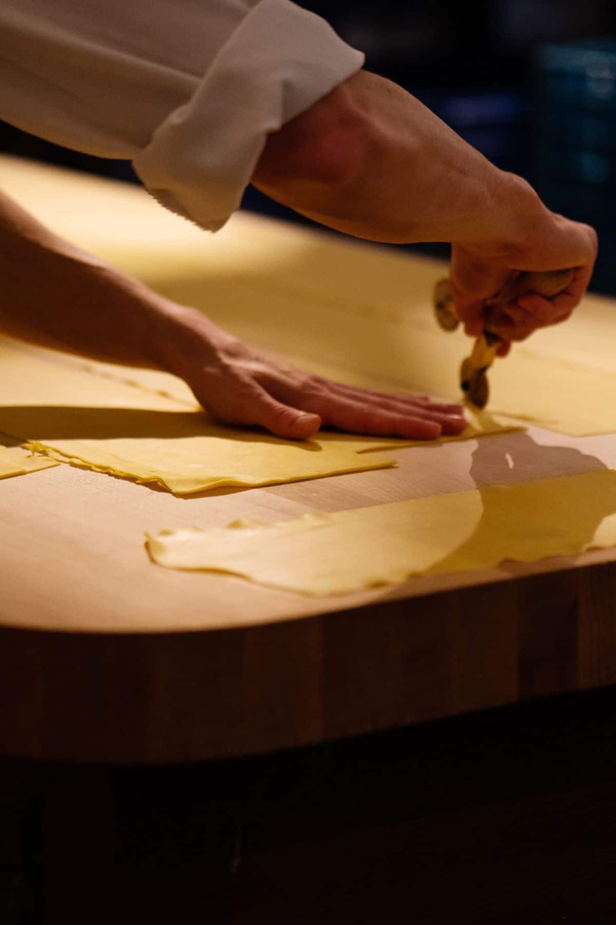 Chef cutting pasta on a wooden table. 