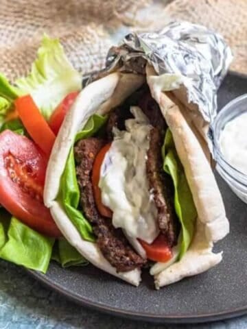 A gyro filled with meat, lettuce, tomatoes, and tzatziki sauce.