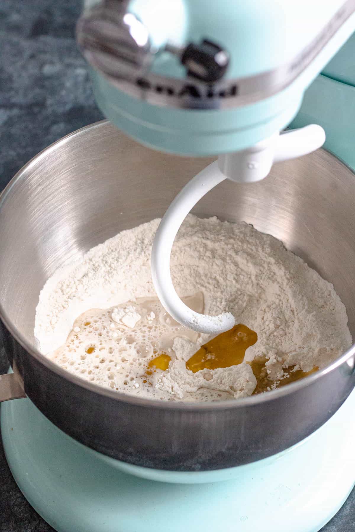 Bread hook on the kitchen mixer with the ingredients added to the mixing bowl to knead. 