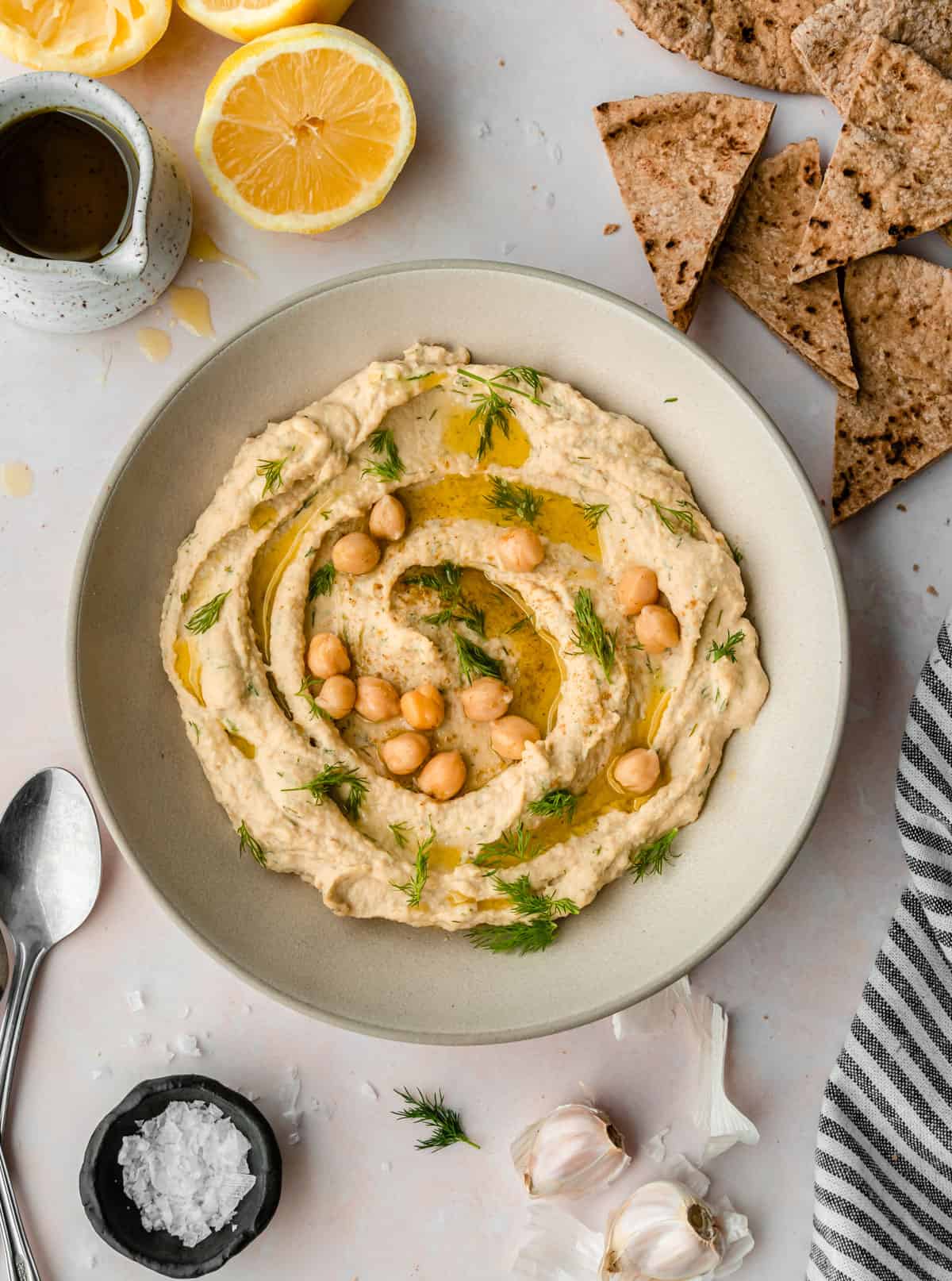 Lemon dill hummus garnished with fresh dill, whole chickpeas and chips around the bowl. 