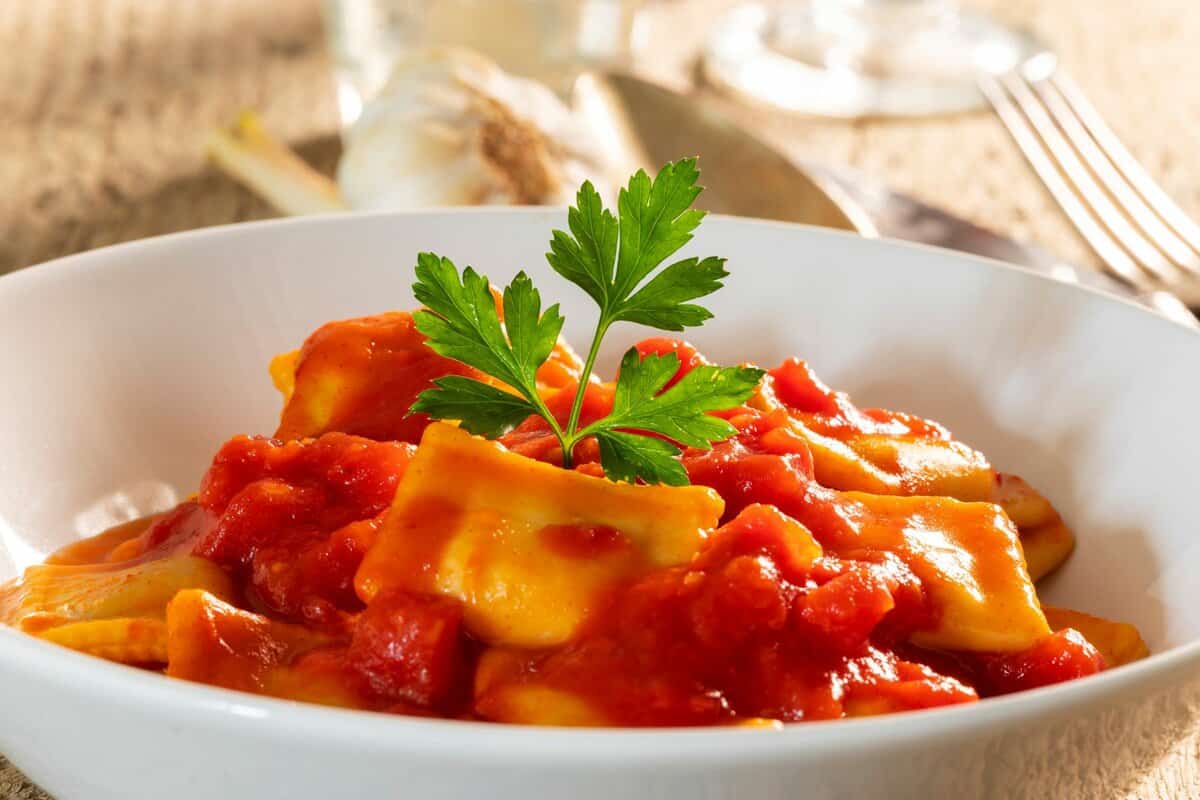 Bowl of ravioli with pasta sauce over it and fresh parsley garnished on top. 