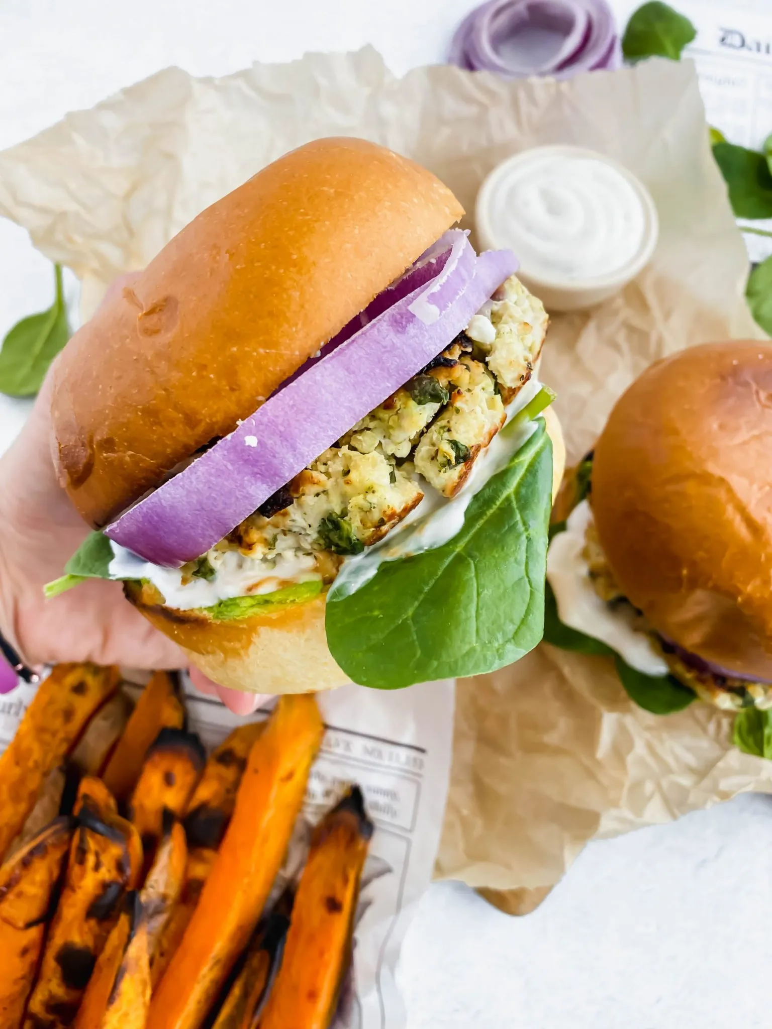 A spinach feta turkey burger being held up by a hand with sweet potato fries served alongside. 