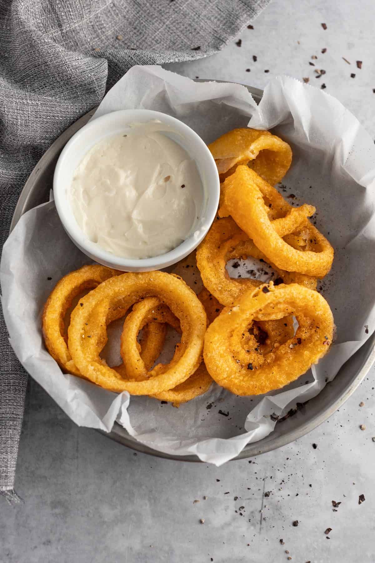 Air Fryer Frozen Onion rings laying on parchment paper with a small bowl of dipping sauce. 