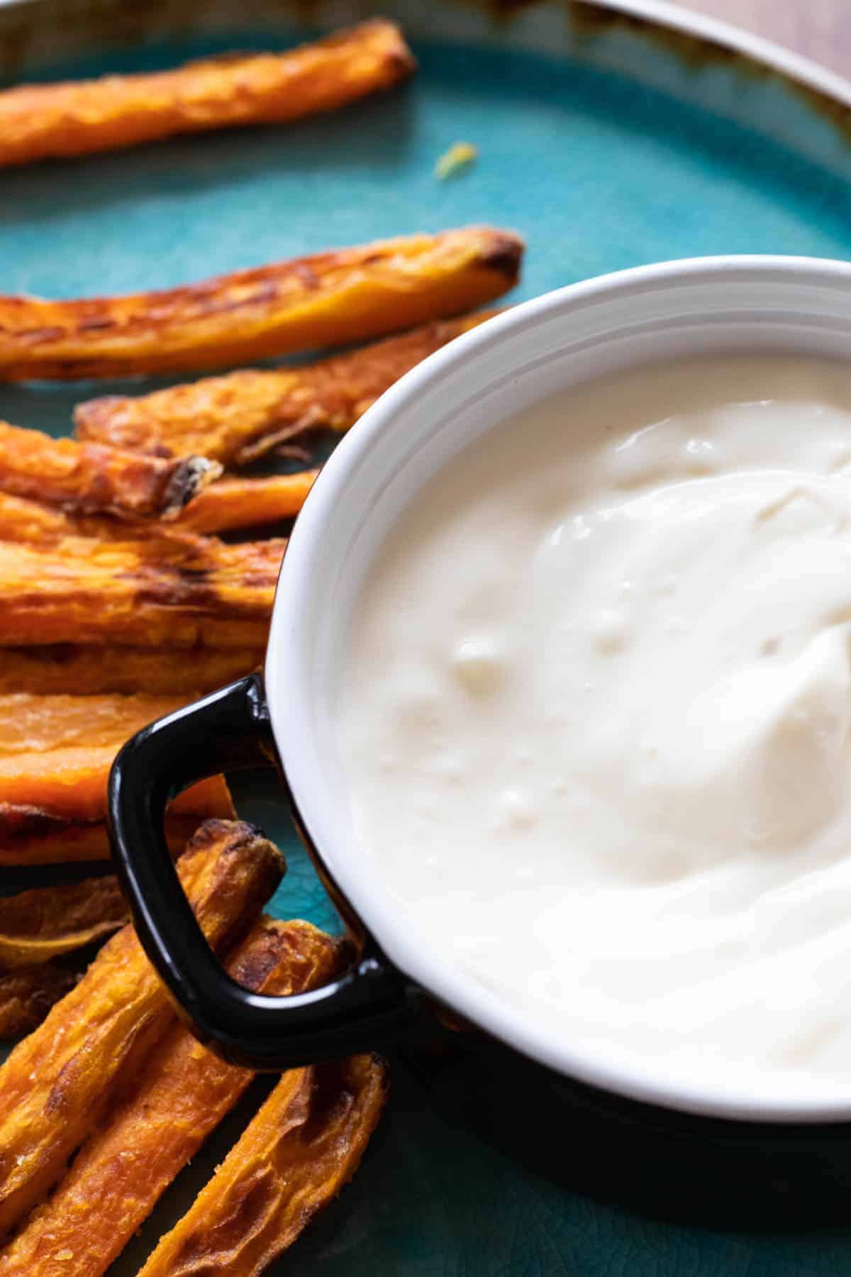 Garlic dipping sauce in a bowl with some sweet potato fries laying besides the bowl. 