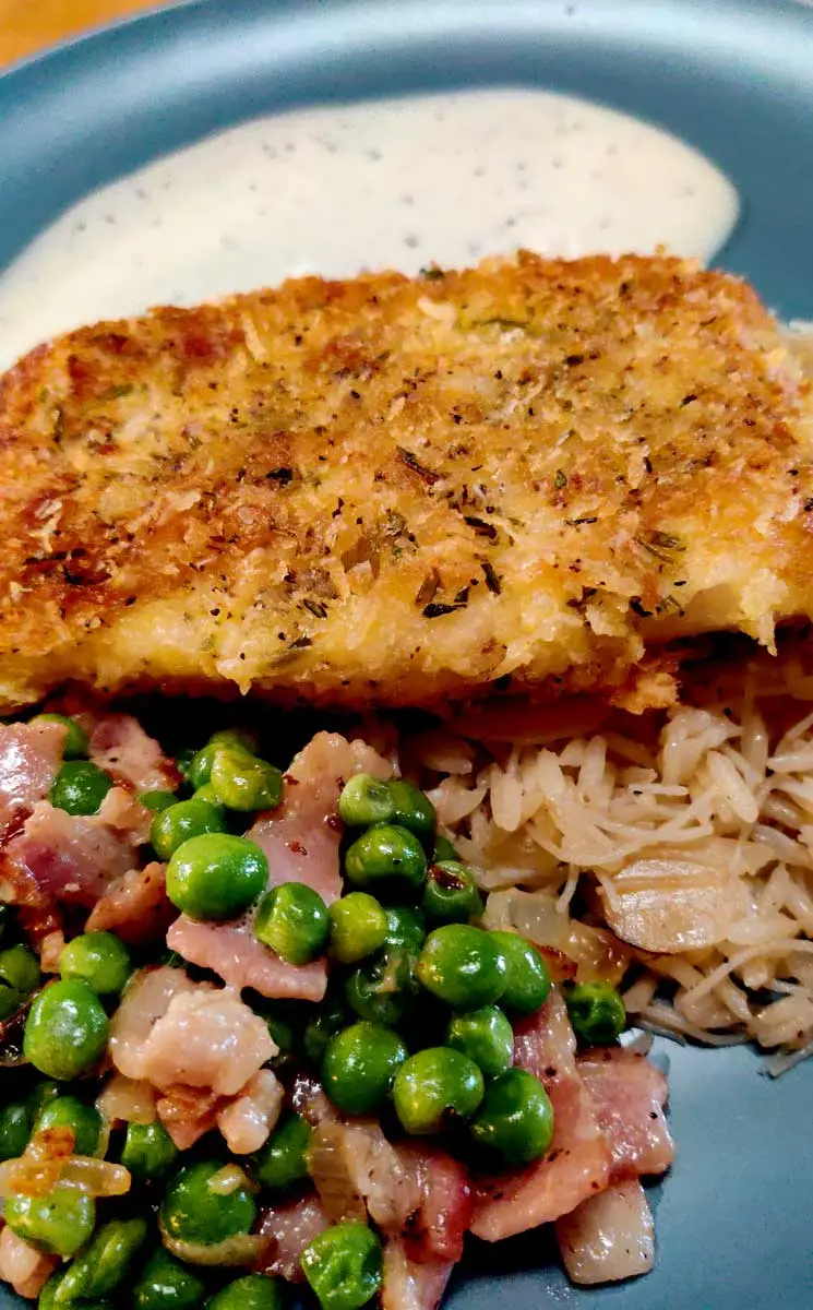 Parmesan crusted cod on a plate with bacon and peas. 