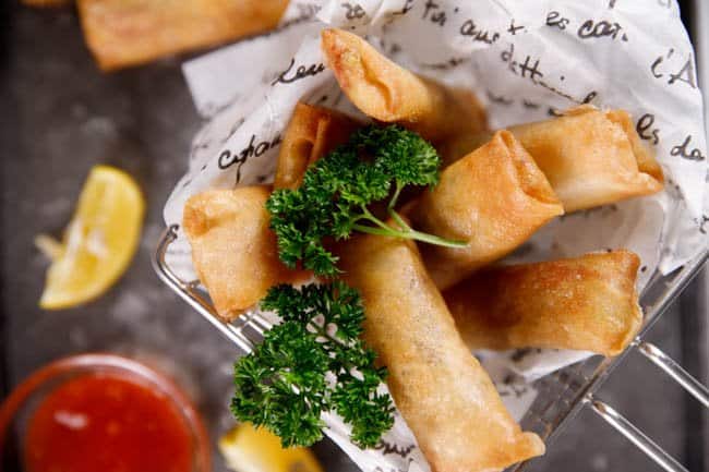 Chinese spring rolls in a basket sitting on parchment paper. 