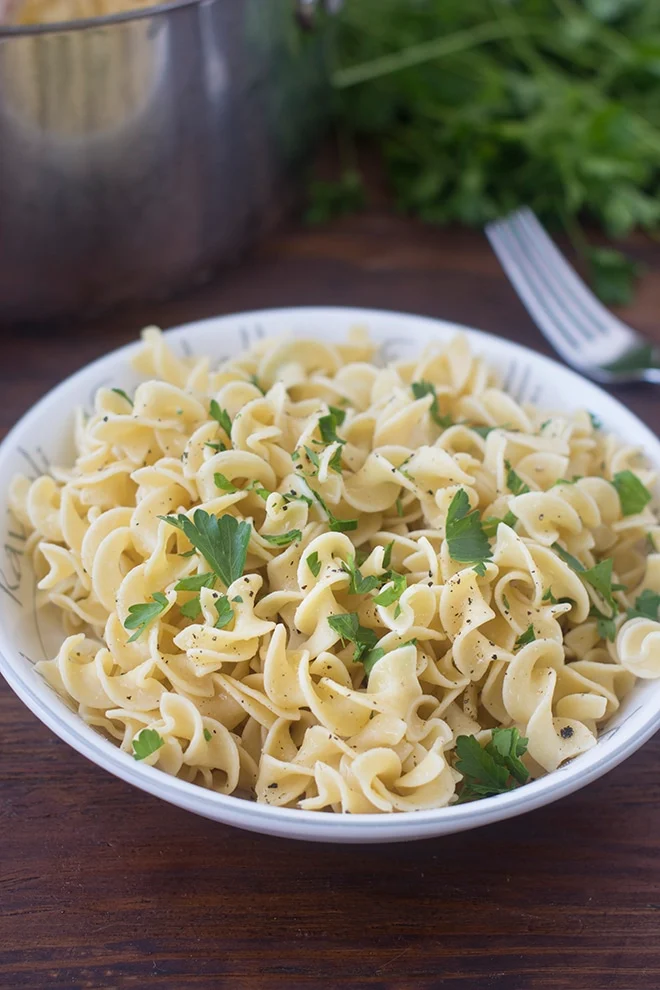 Buttered egg noodles in a bowl and topped with parsley.