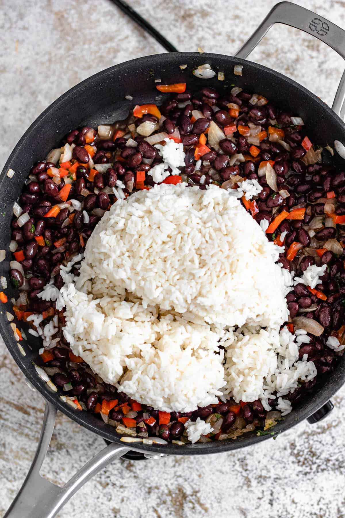 Leftover white rice added to the top of black beans and sauteed veggies in a frying pan. 