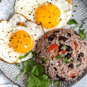 A plate with a mound of Gallo Pinto, two fried eggs, and some cilantro leaves.