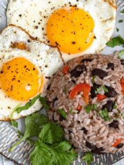 A plate with a mound of gallo pinto, two fried eggs, and some cilantro leaves.