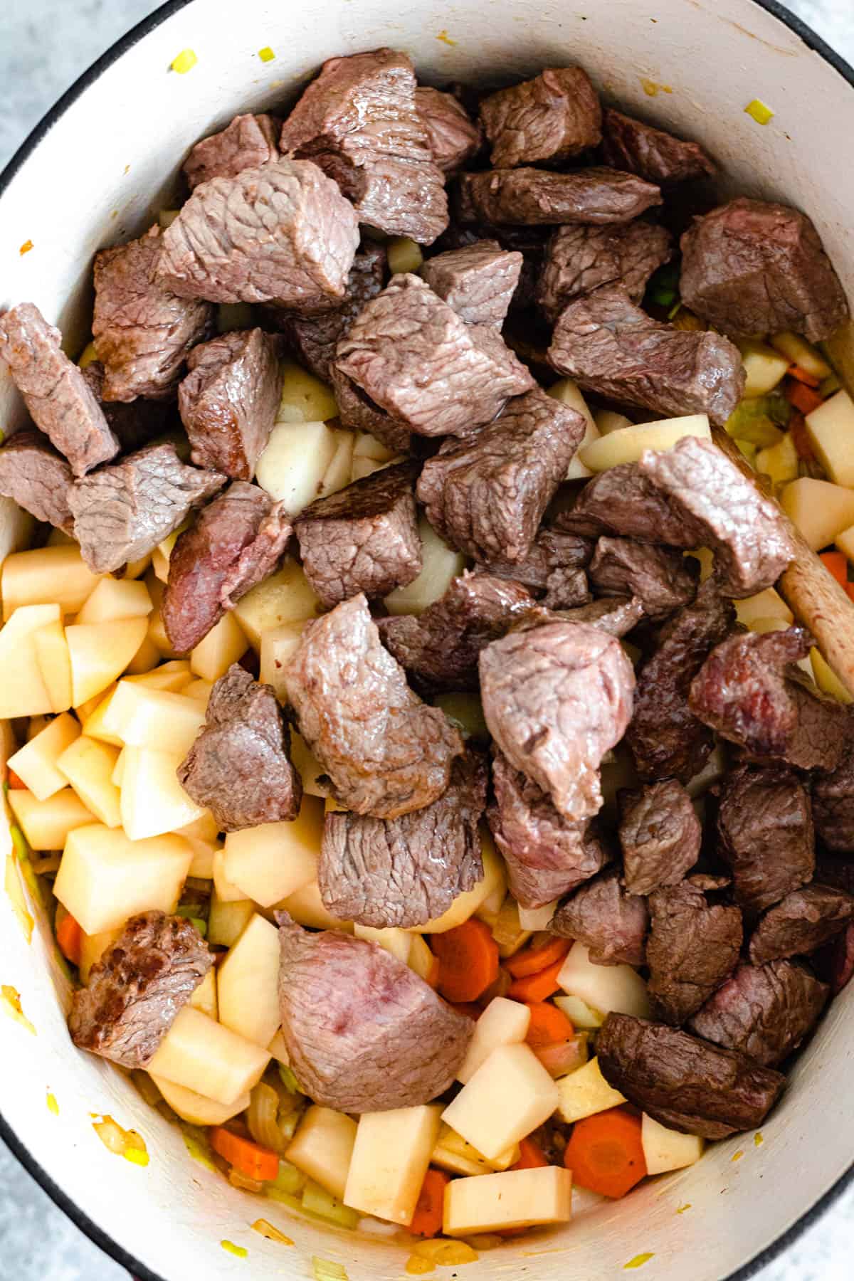 Potatoes, beef stew meat and veggies combined in a Dutch oven to prepare Irish stew recipe. 