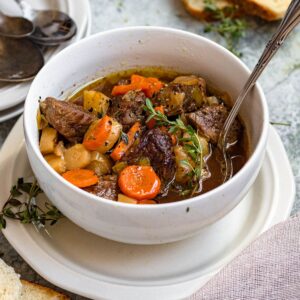 Irish stew in a bowl with carrots, beef, potatoes, and thyme with a spoon sticking out of the top.