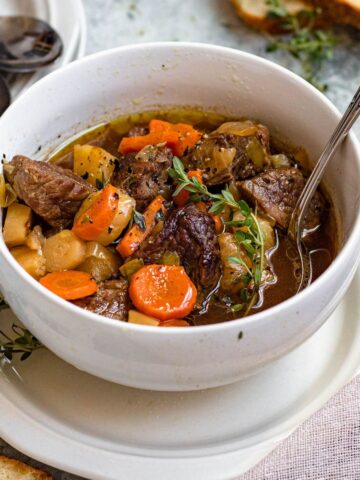 Irish stew in a bowl with carrots, beef, potatoes, and thyme with a spoon sticking out of the top.