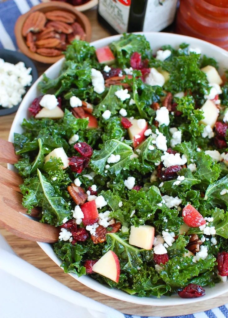 A bowl with wooden salad tongs of kale salad with cranberries. 