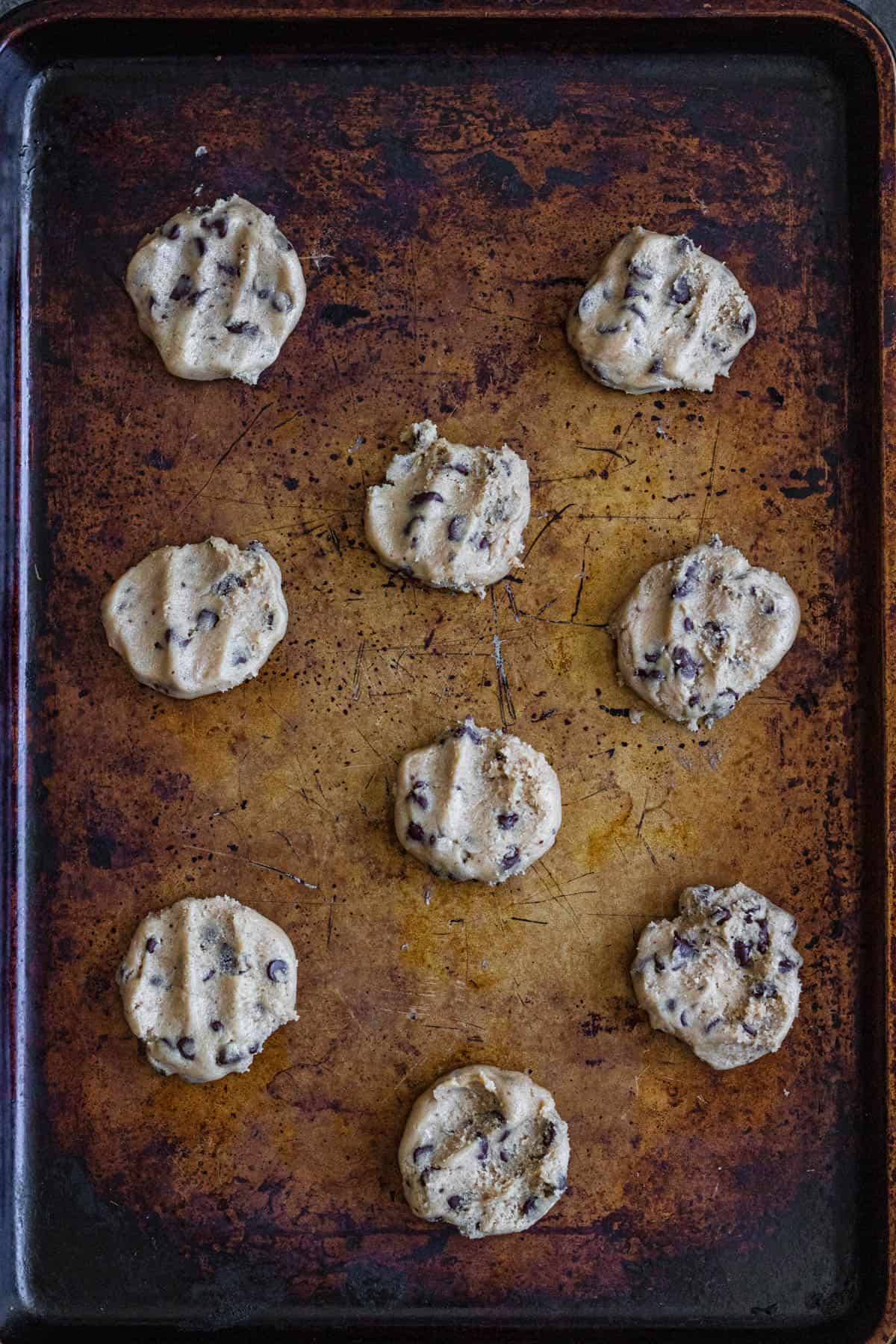 Chocolate chip cookie dough flattened a bit and laying on a baking sheet. 