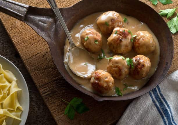 Small pan with swedish meatballs and gravy sitting on a wooden cutting board. 