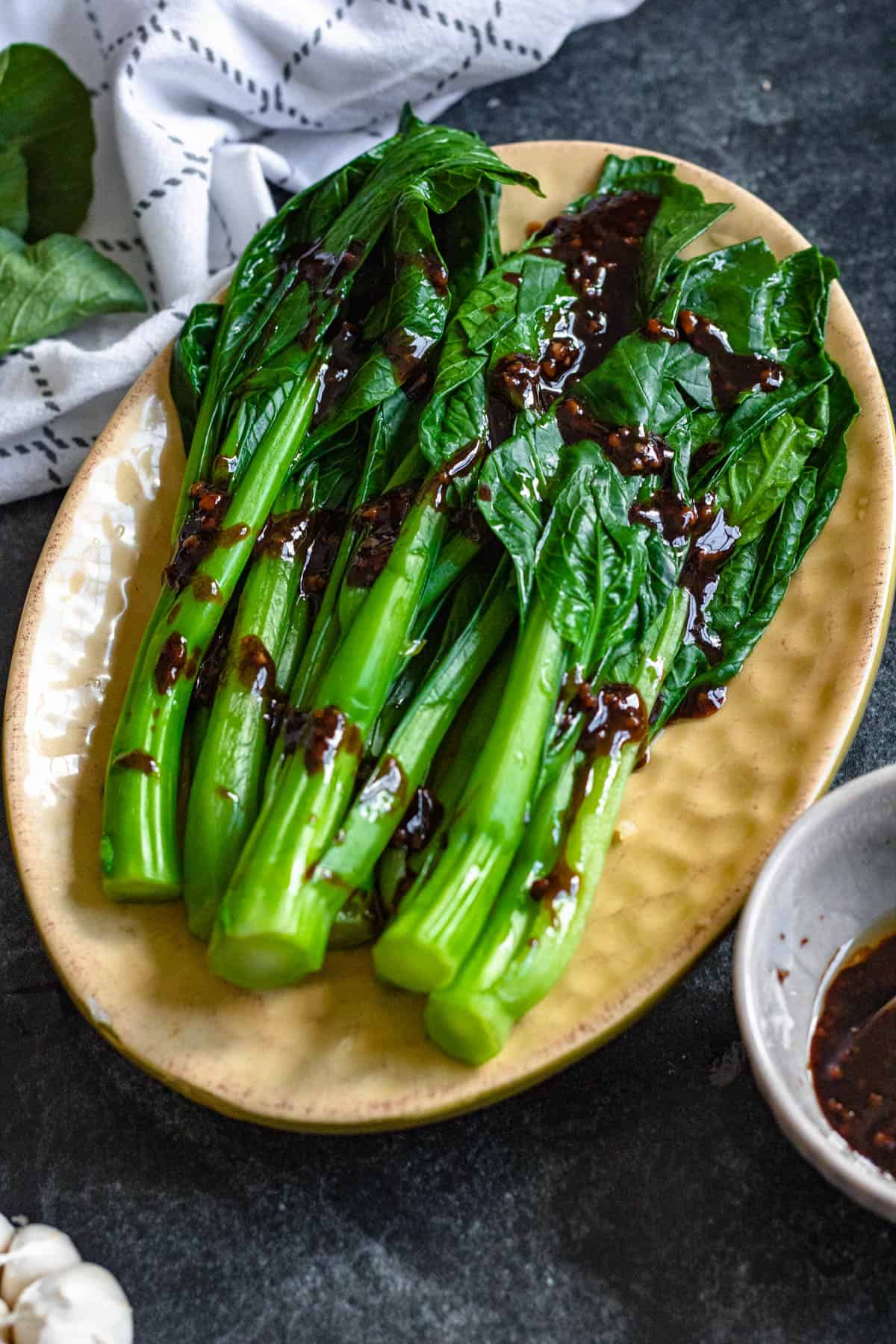 Yu choy served on a plate with a sauce drizzled over the top. 