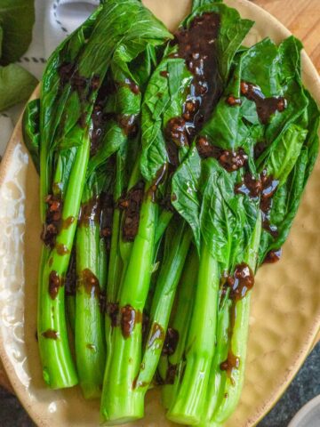 Steamed Yu Choy Sum on an oval plate drizzled with sauce.
