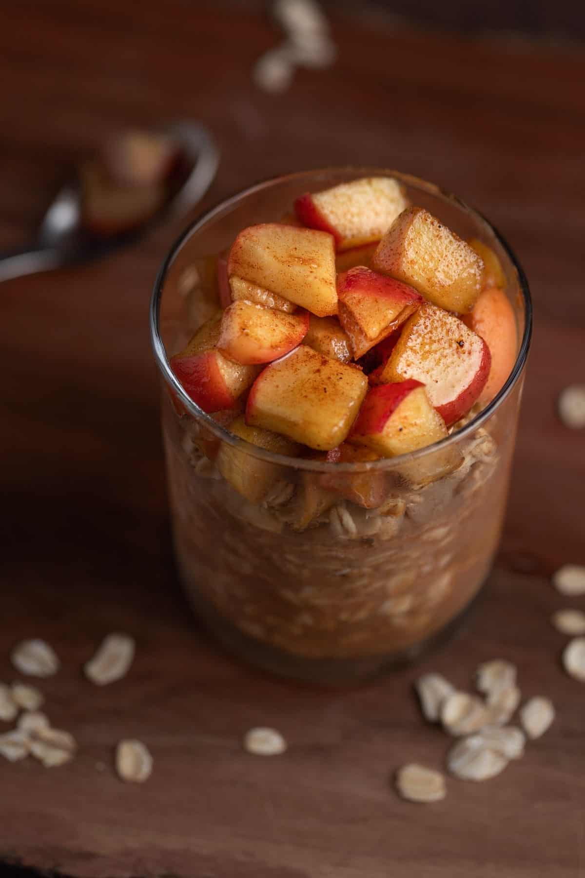 Apple pie overnight oats with diced apples on top served in a glass.