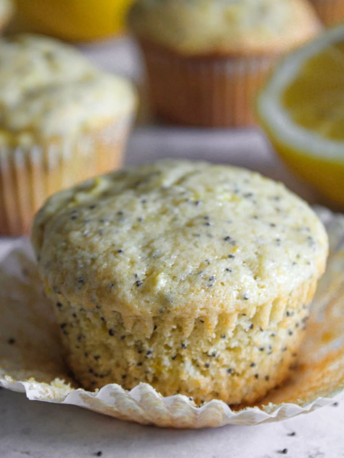 Lemon poppyseed muffin with yellow squash sitting on the wrapper that is pulled away from the edges. 