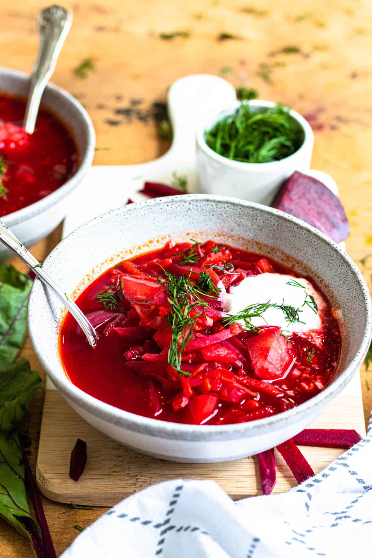 Close up bowl of borscht soup topped with sour cream and dill weed 