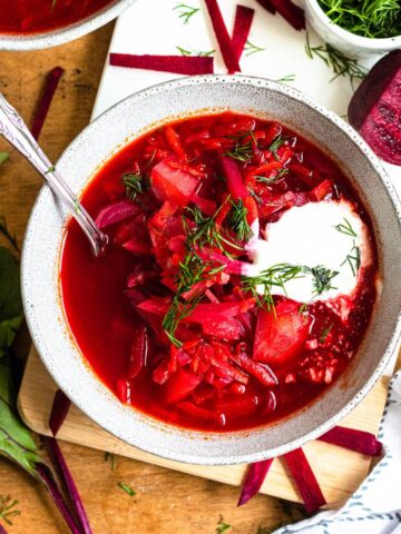 Bowl of vegetarian Borscht with a dollop of cream and fresh dill served on top.