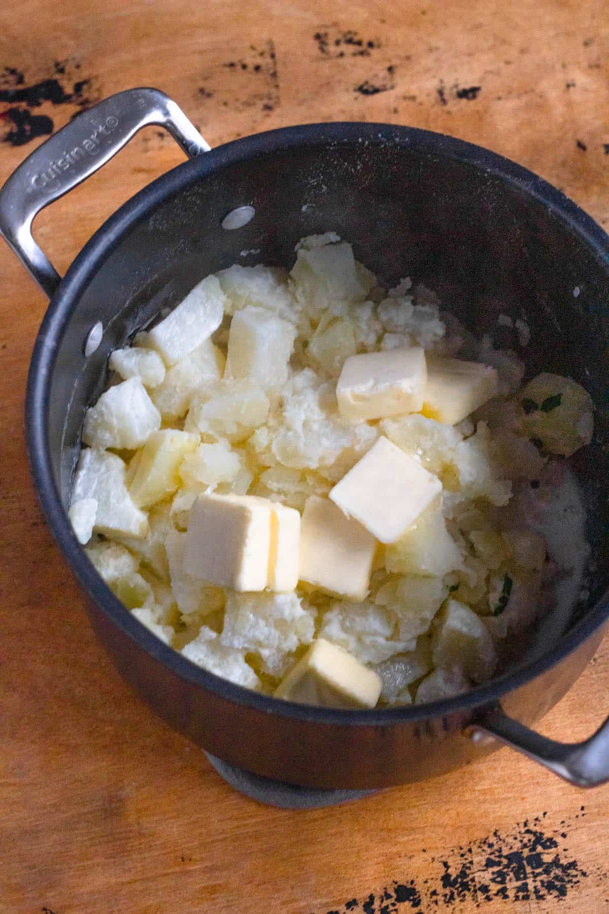 Pats of butter added to  the top of mashed potatoes in a pan. 