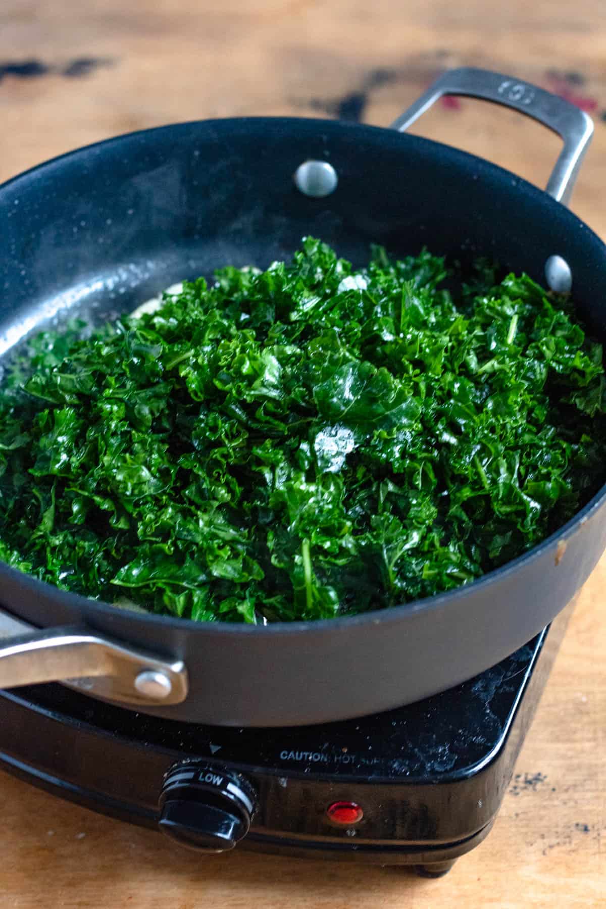Kale sauteing in bacon grease in a frying pan. 