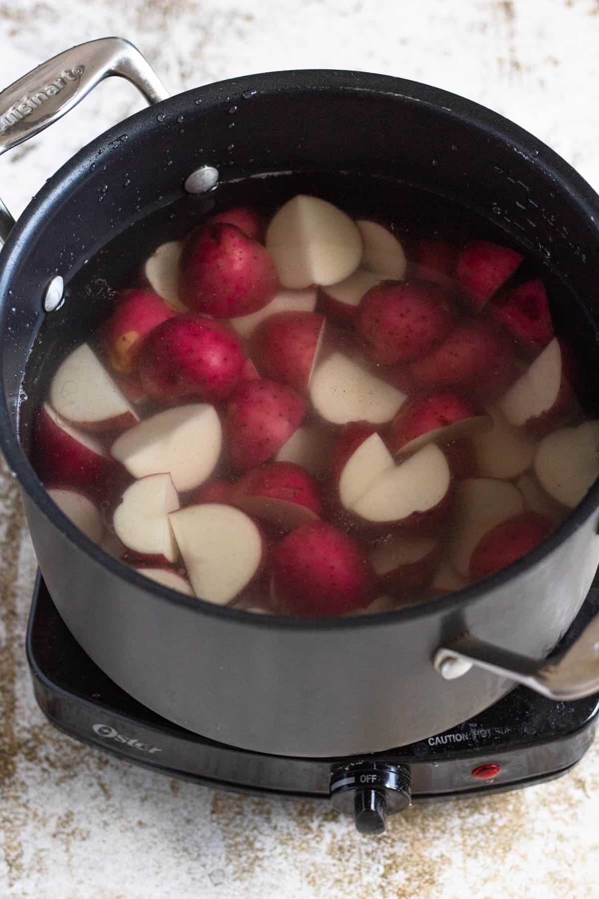 Pot of water with chunks of red potatoes submerged. 