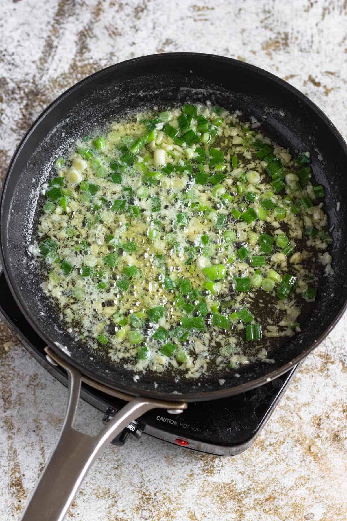 Butter, garlic and green onions sauteing in a frying pan. 