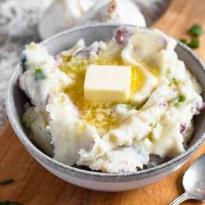 A pat of butter melting over a bowl of garlic redskin mashed potatoes with a spoon on the side.