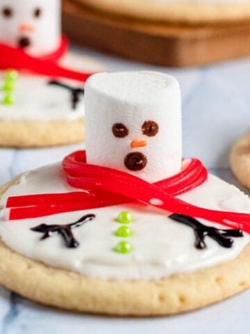 Melted snowman cookies with a marshmallow head and a licorice scarf.