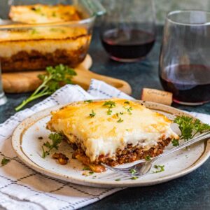 A plate of Moussaka sitting in front of glasses of wine and a pan of moussaka with fork sitting in front of it.