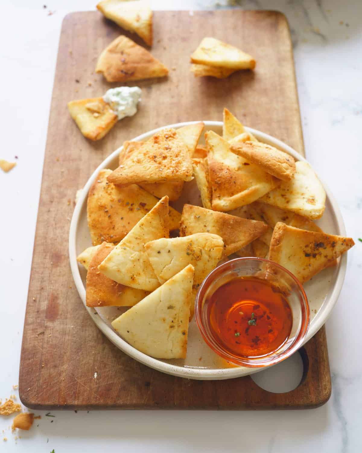 Air Fryer pita chips in a bowl sitting on a cutting board with a side of dipping sauce. 