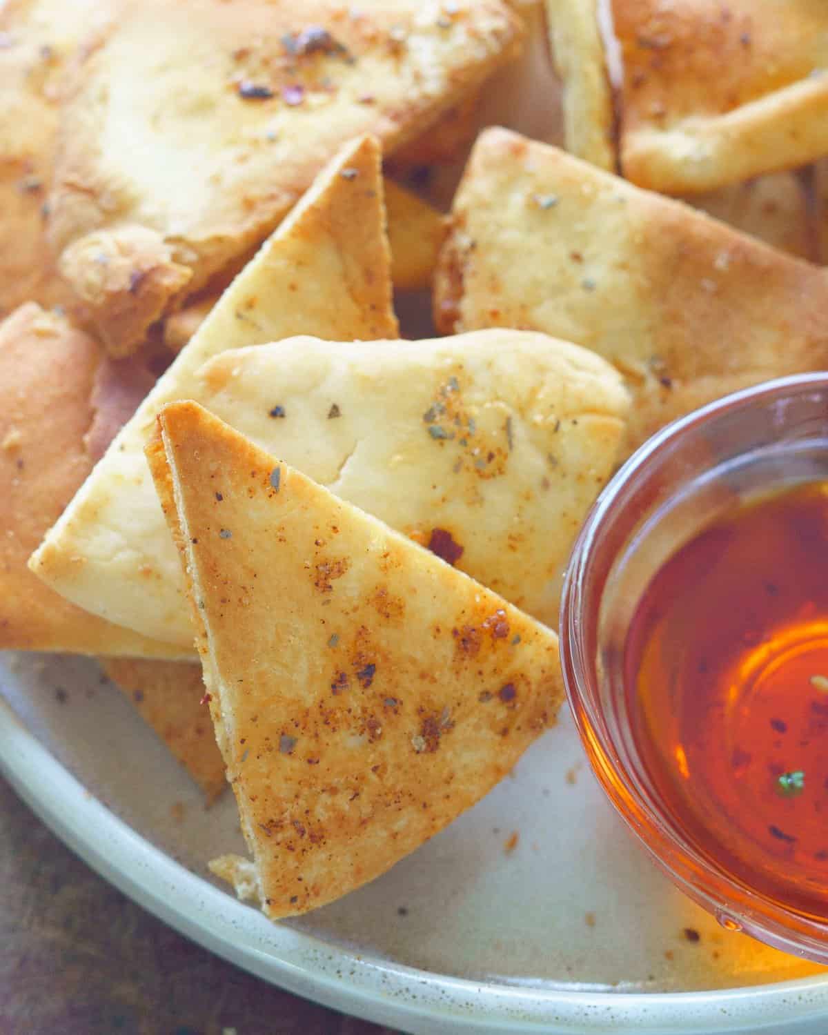 Air fryer pita chips on a plate with a side of sauce. 