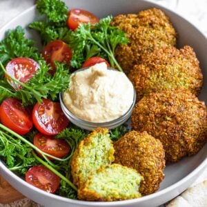 A bowl of falafel with parsley, tomatoes, and a scoop of hummus.