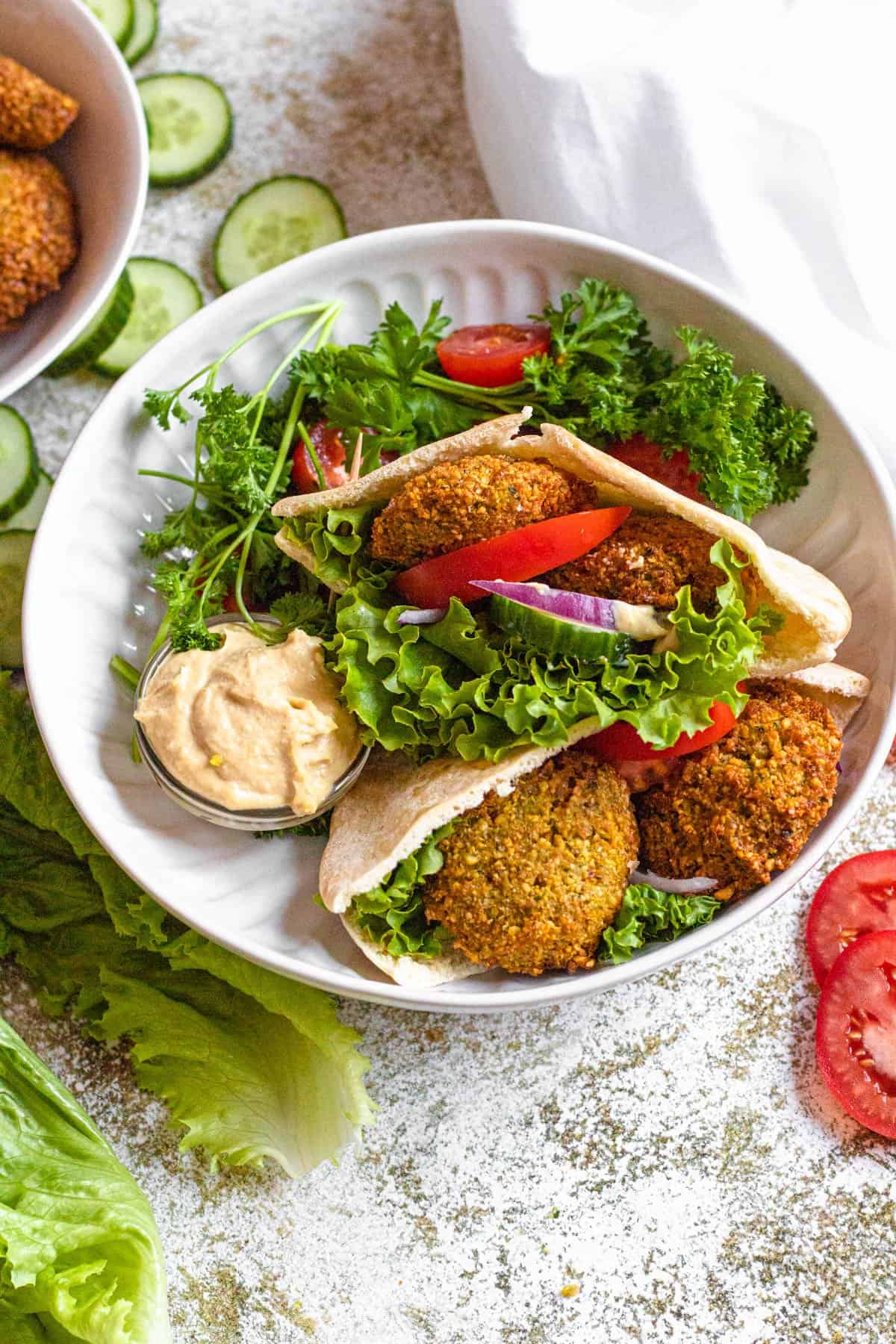 Bowl of falafel pitas with chopped cherry tomatoes and parsley garnishes. 
