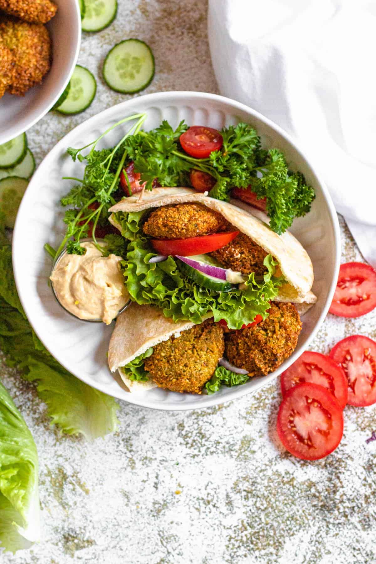 Falafel pitas served in a bowl with garnish of parsley, cherry tomatoes and hummus on the side. 