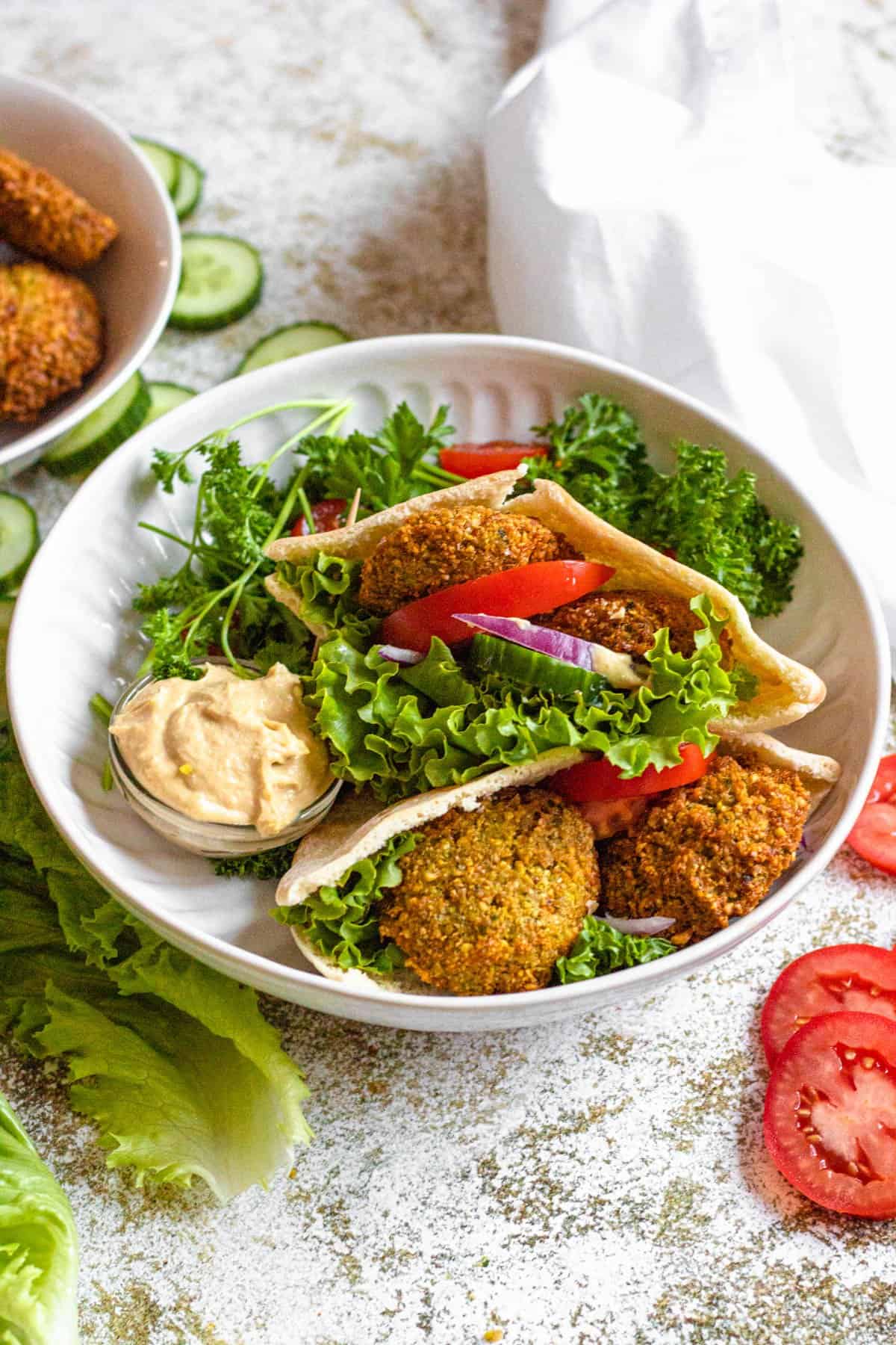 Bowl of falafel pita sandwiches with a small dish of hummus to serve with it. 