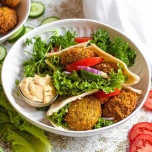 Falafel pita in a serving bowl served with tomatoes, lettuce, and hummus.