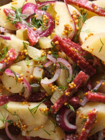 German potato salad with fresh herbs, red onions, mustard seeds, and dressing.