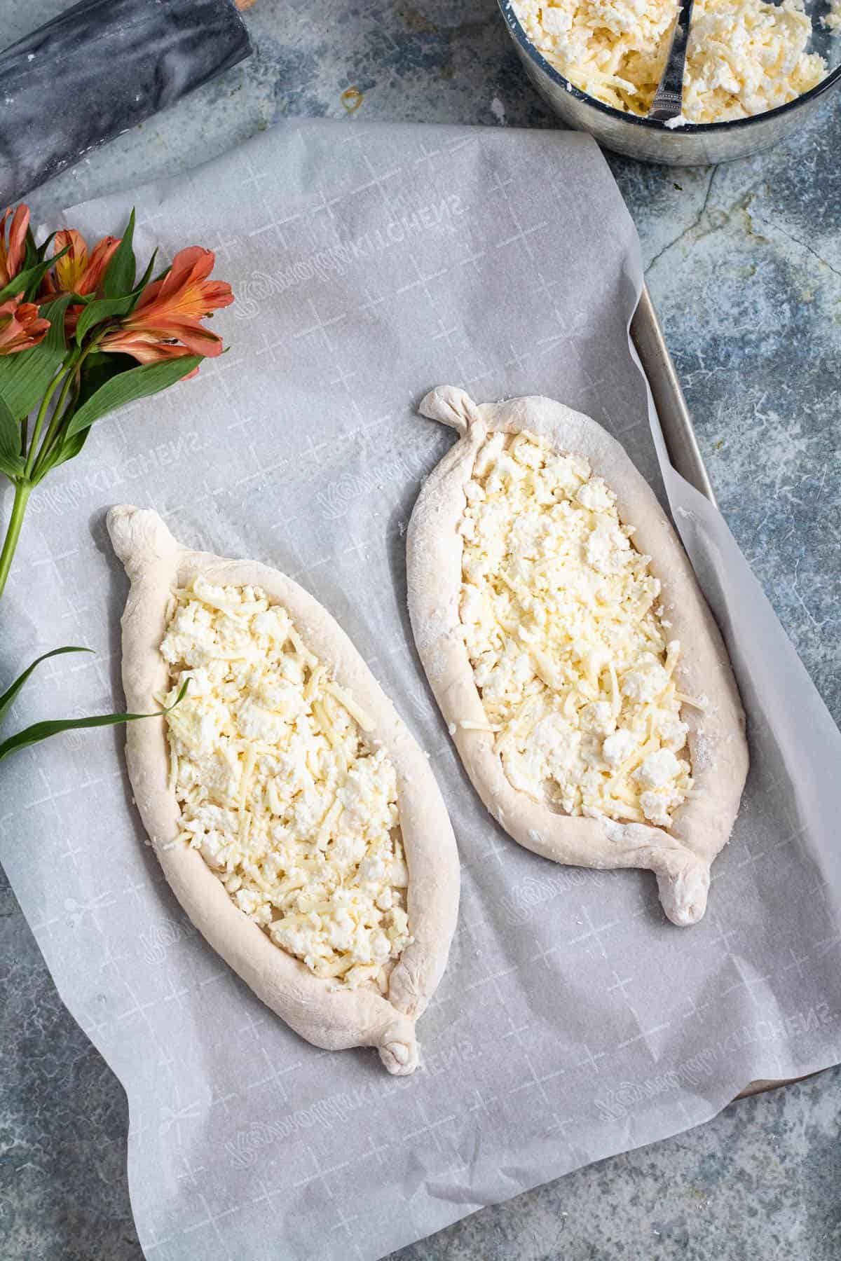 Dough rolled out and shaped to make khachapuri with cheese sprinkled in the middle. 