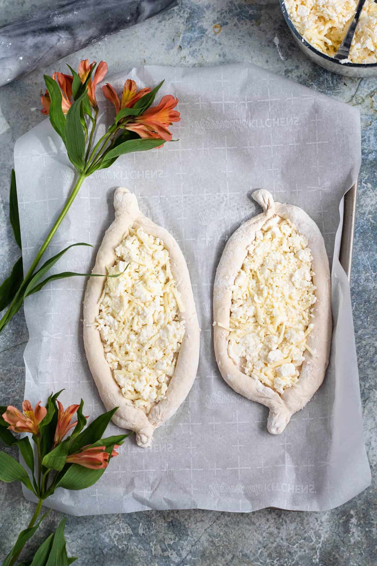 Dough rolled out and shaped to make khachapuri with cheese sprinkled in the middle surrounded by flowers.