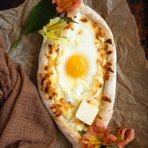 Kachapuri bread boat topped with an egg and butter on parchment paper, surrounded by flowers.