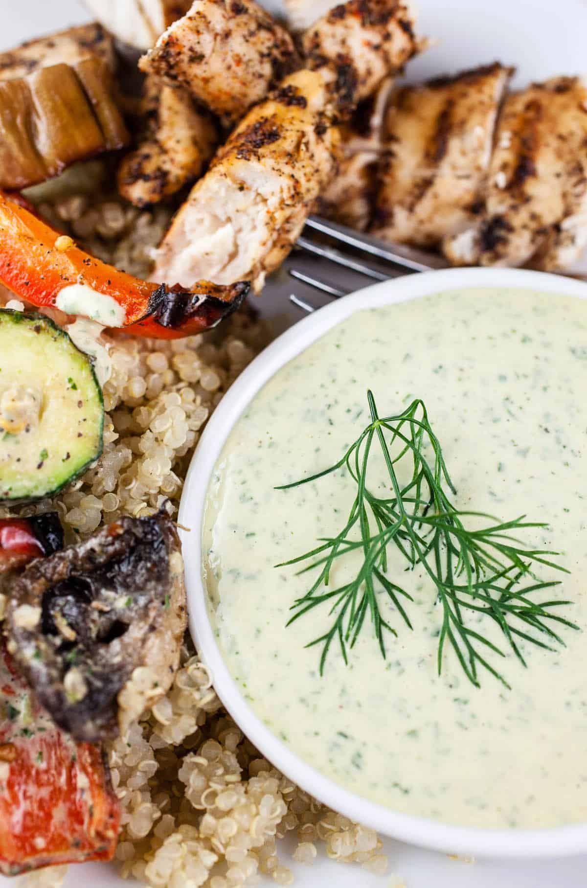 Lemon Herb tahini sauce in a bowl with grilled chicken skewers and roasted veggies alongside it. 