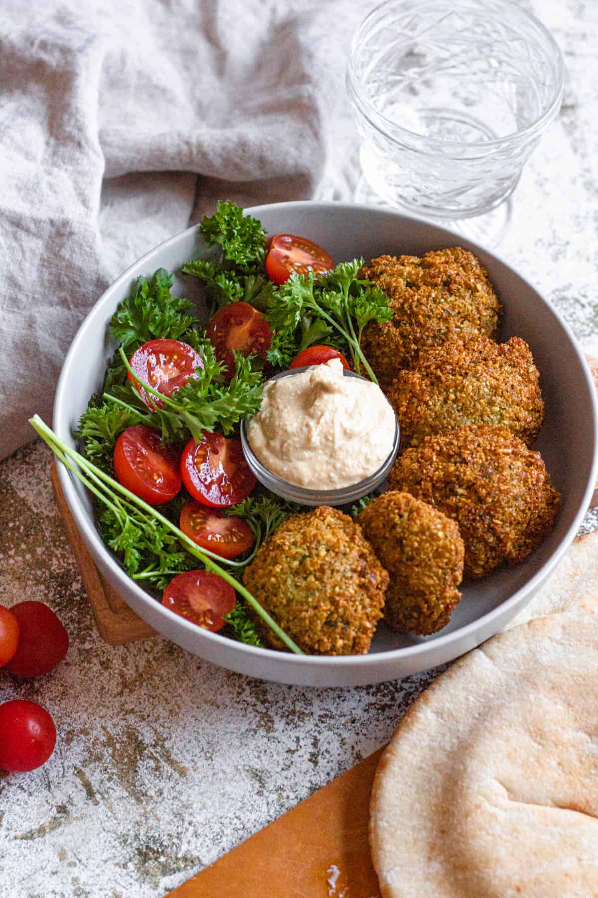 Top view of middle eastern falafel recipe on a plate with cherry tomatoes cut in half and dipping sauce in a small container in the middle. 