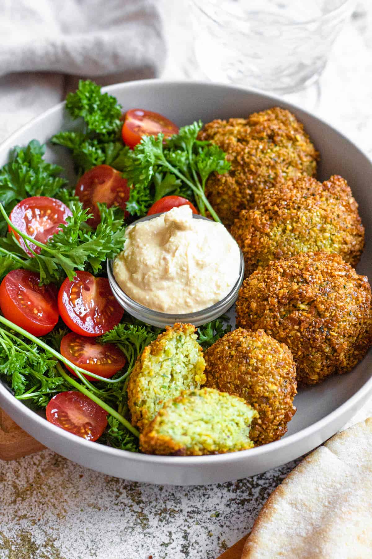 Bowl of fried falafel balls and a side of dip and halved cherry tomatoes. 