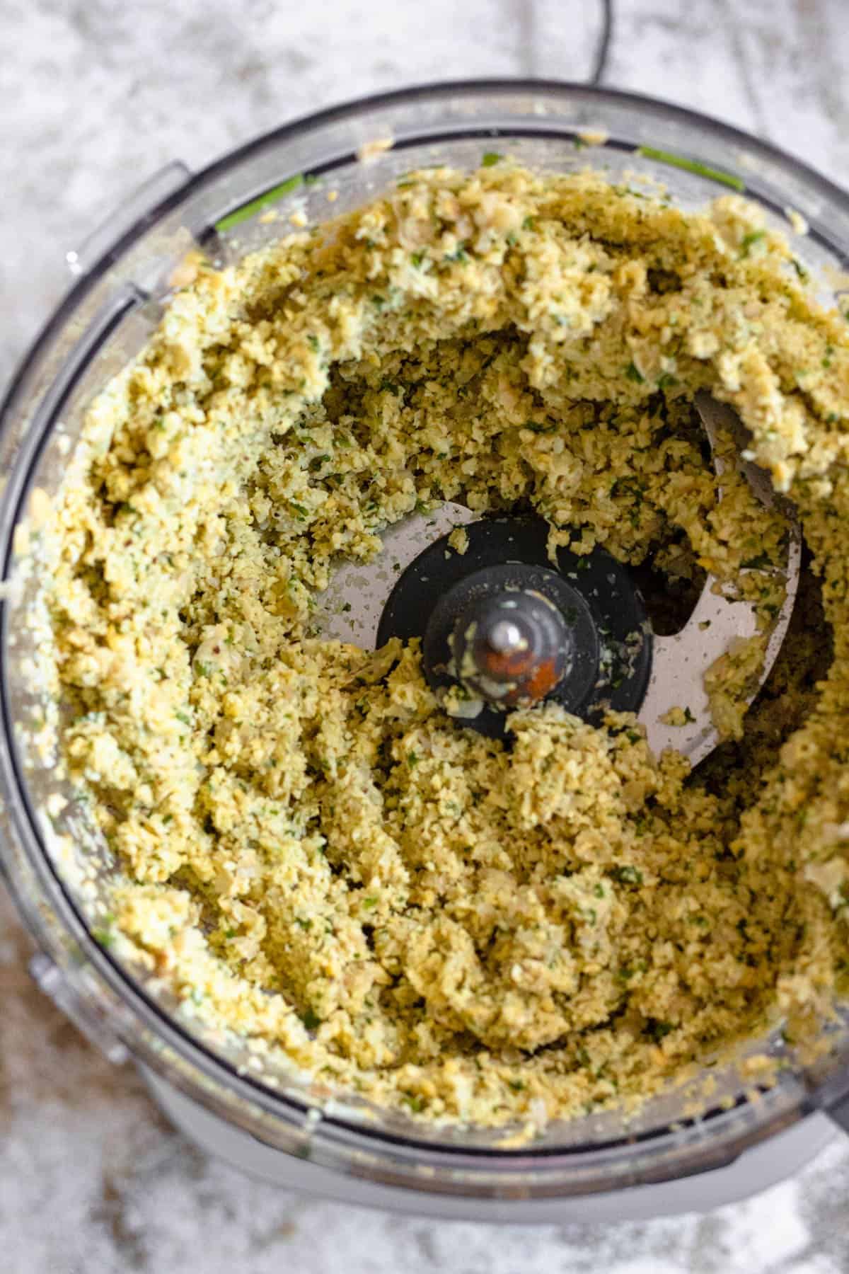 Food processor with falafel mixture combining with seasonings. 