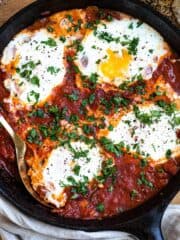 Shakshuka in a cast iron skillet topped with cooked eggs and parsley.