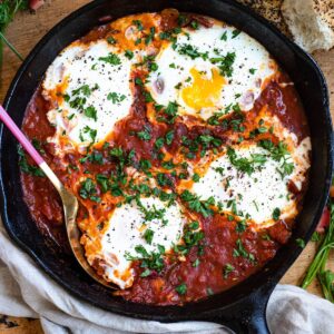 Shakshuka in a cast iron skillet topped with cooked eggs and parsley.